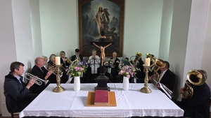 Mitglieder des Posaunenchores sitzen auf Stühlen kreisförmig hinter dem Altar und blasen auf ihren Instrumenten.